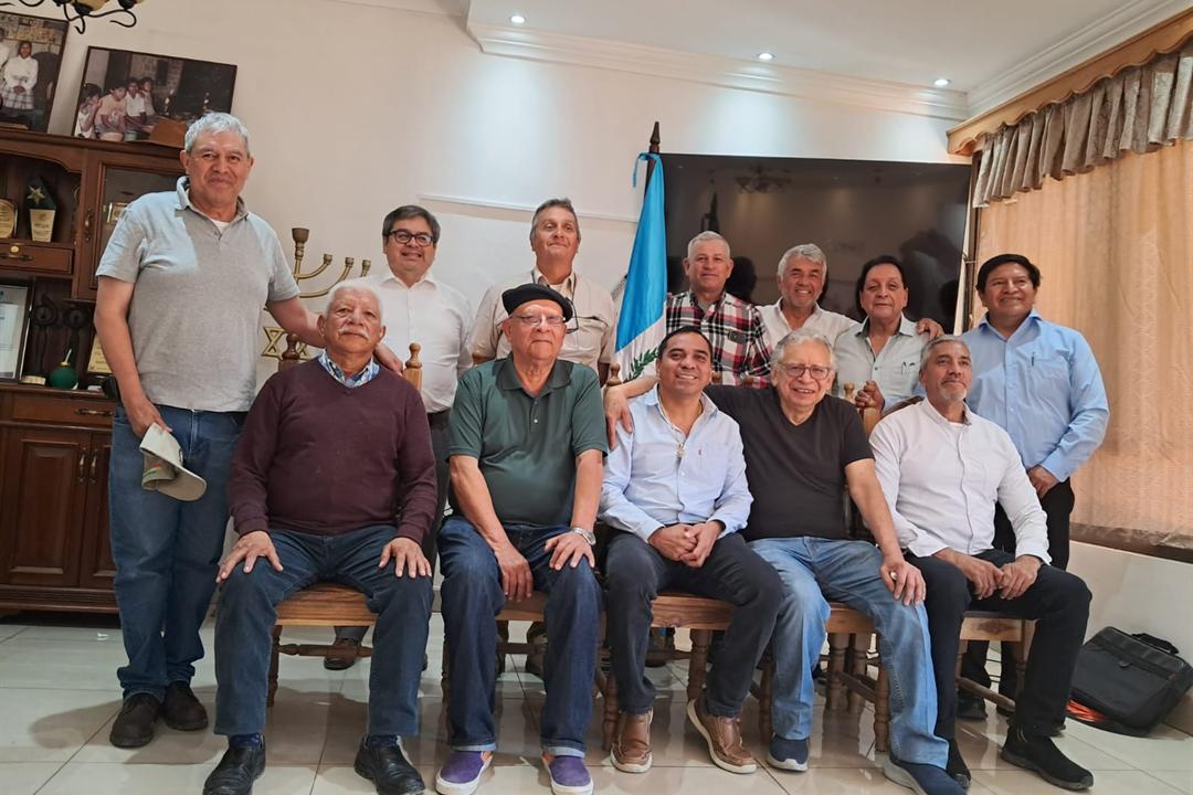 La Junta Directiva y los órganos de la AGK reunidos durante la visita al terreno donado, junto a la bandera de Guatemala